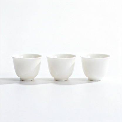 Set of three white handleless ceramic tea cups with flared rims and rounded feet on a white background