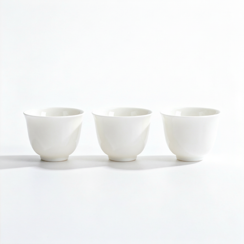 Set of three white handleless ceramic tea cups with flared rims and rounded feet on a white background