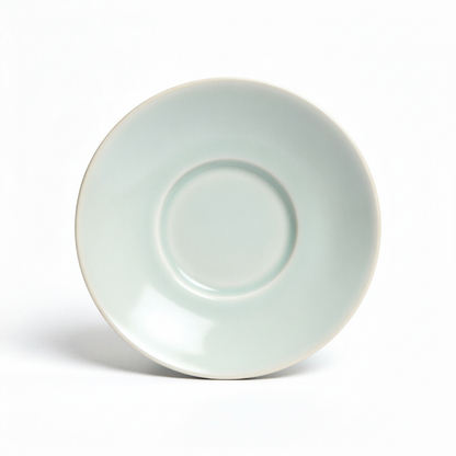 Pale celadon-white ceramic tea saucer with a central support ring on a white background